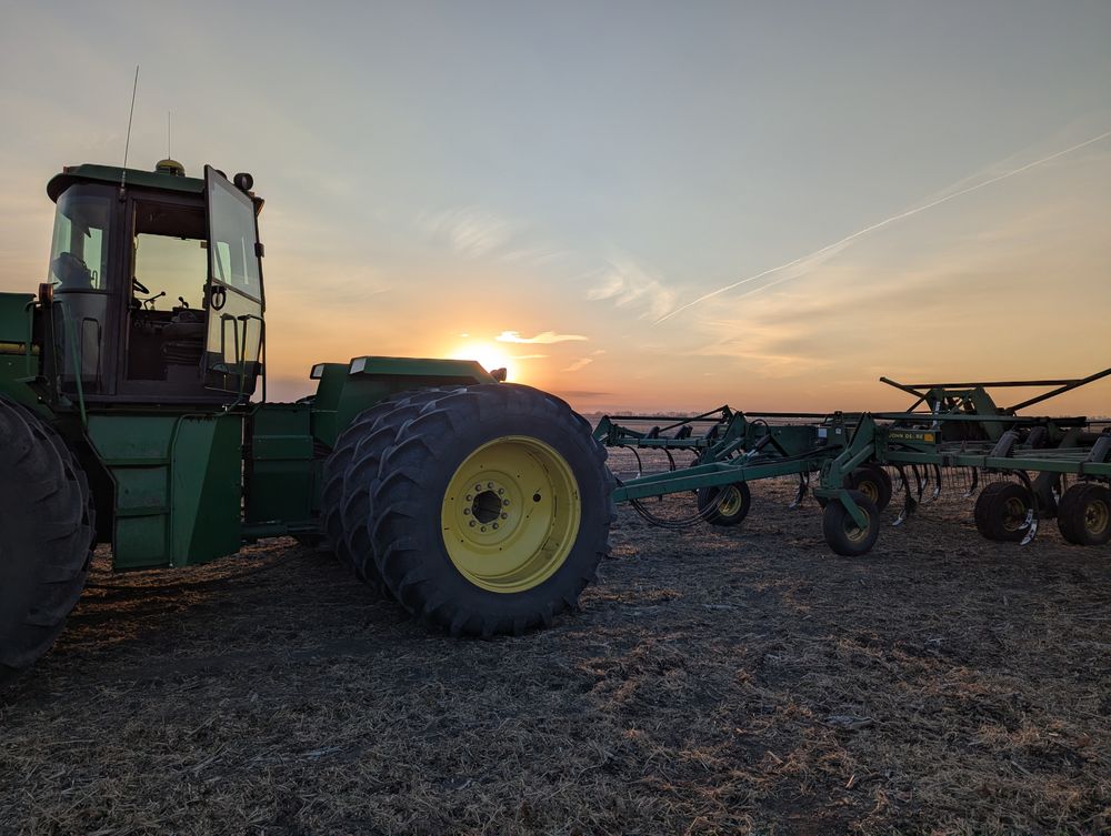 John Deere tractor and field cultivator in a tilled field at sunset